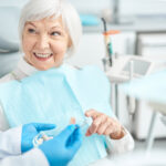 An image of an older woman sitting in a dental chair after a dental implant procedure.